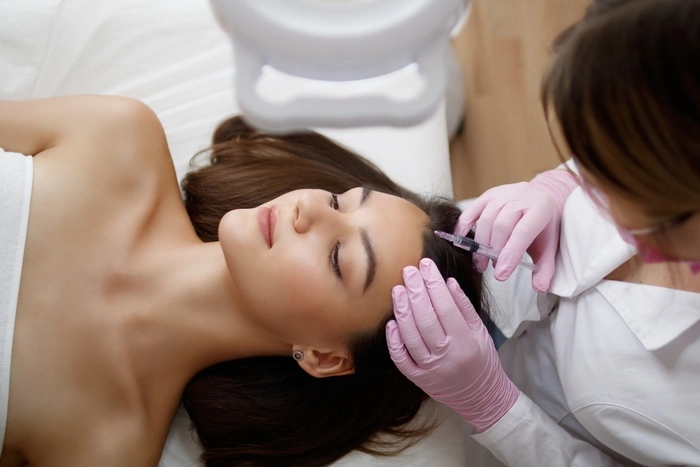 Young beautiful woman receiving hair mesotherapy injections from a professional trichologist.