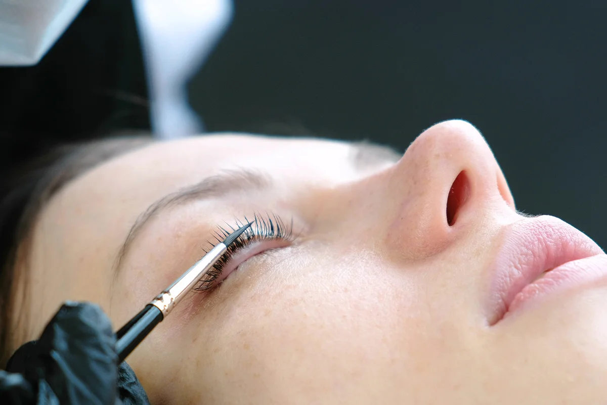 A closed-eye view of a woman receiving a lash lift procedure with a silicone lifting rod applied to her eyelid.