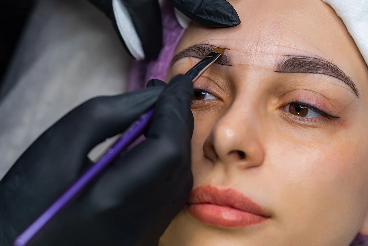 Aesthetician using a dermaplaning blade to shape a client's eyebrow.